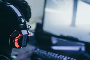 Persona con audífonos gamer jugando videojuegos en el computador.