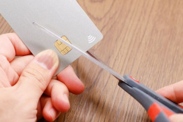 Persona corta una tarjeta de crédito con unas tijeras negras.