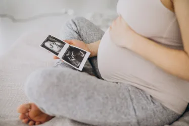 Ilustración gratuita de mujer embarazada con foto de ultrasonido sentada en la cama.