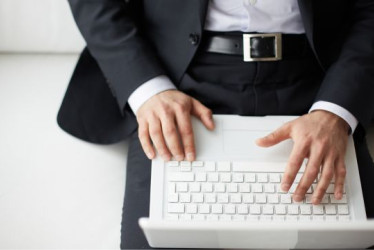 Hombre elegante con un computador portatil blanco en sus piernas.