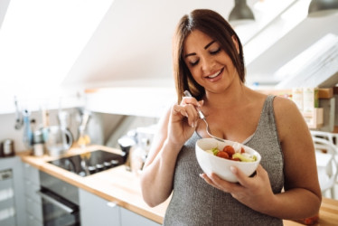Mujer embarazada comiendo de un bowl en una cocina.