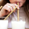 Mujer bebe leche de un vaso con un pitillo que sostiene con una mano.