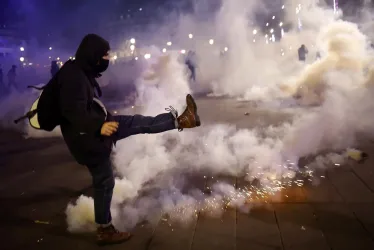 Un manifestante enmascarado lanza un bote de gas lacrimógeno a las fuerzas policiales en la Plaza de la República, durante una manifestación contra la reforma de las pensiones del gobierno en París, Francia, este martes.