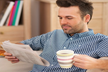 Hombre sonriente leyendo el periódico con una taza de café.