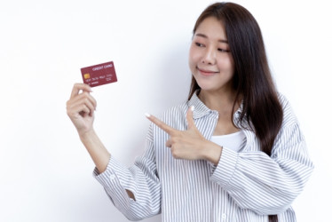 Mujer sostiene una tarjeta de crédito con una mano y la señala con la otra.