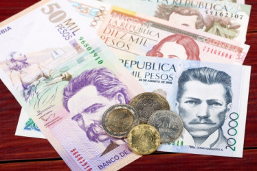 Billetes y monedas de plata colombiana en una mesa de madera.