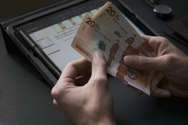 Dos manos contando billetes de 20 mil pesos colombianos con una tablet en el fondo.