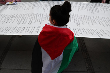Un participante cubierto con una bandera palestina sostiene una pancarta que resume las víctimas del conflicto de Gaza durante una protesta contra la 60ª Conferencia de Seguridad de Munich (MSC), en Munich, Alemania