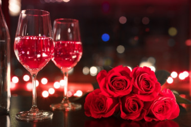 Copas con vino rosado al lado de rosas rojas.